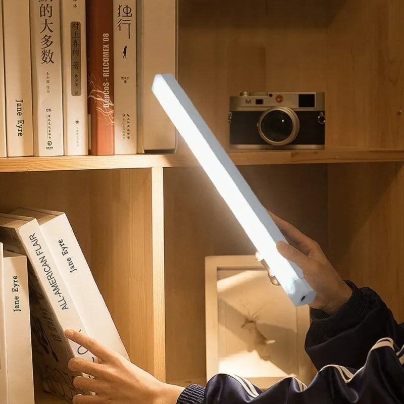 Lámpara LED portátil iluminando estantería de madera con libros y cámara decorativa