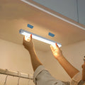 Persona instalando luz LED bajo mueble en un armario, iluminación moderna para hogar