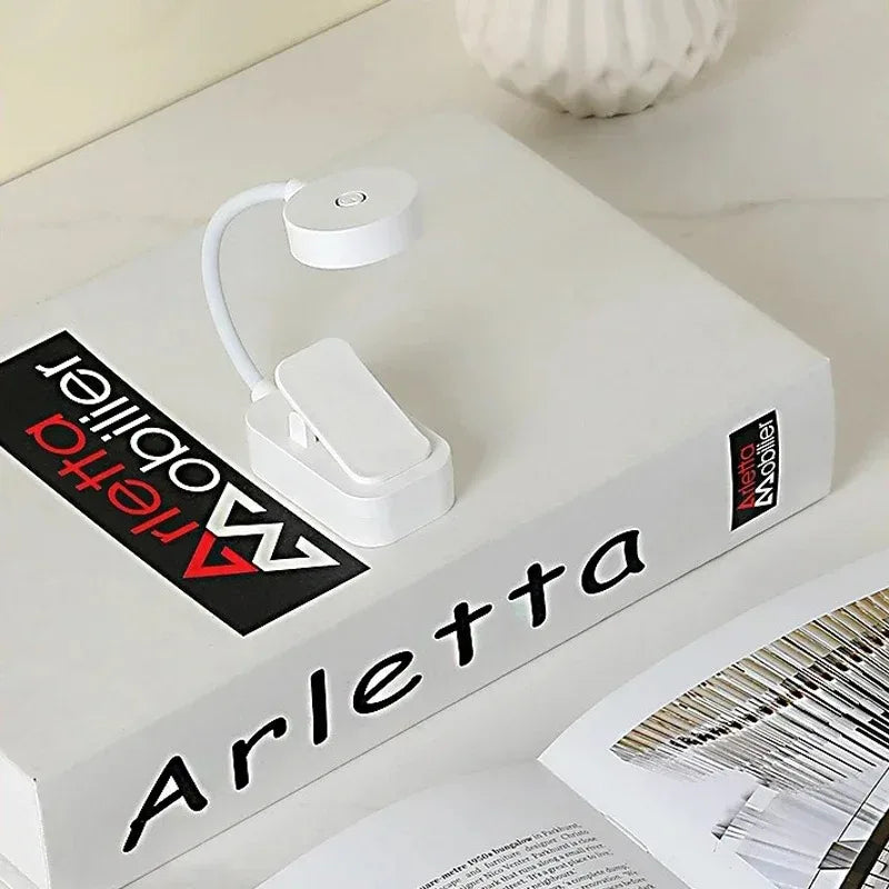 Lámpara LED portátil blanca con clip sobre libro, ideal para lectura y escritorio moderno